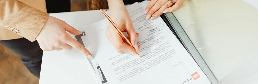 Two women signing important documents at an office desk, showcasing teamwork.